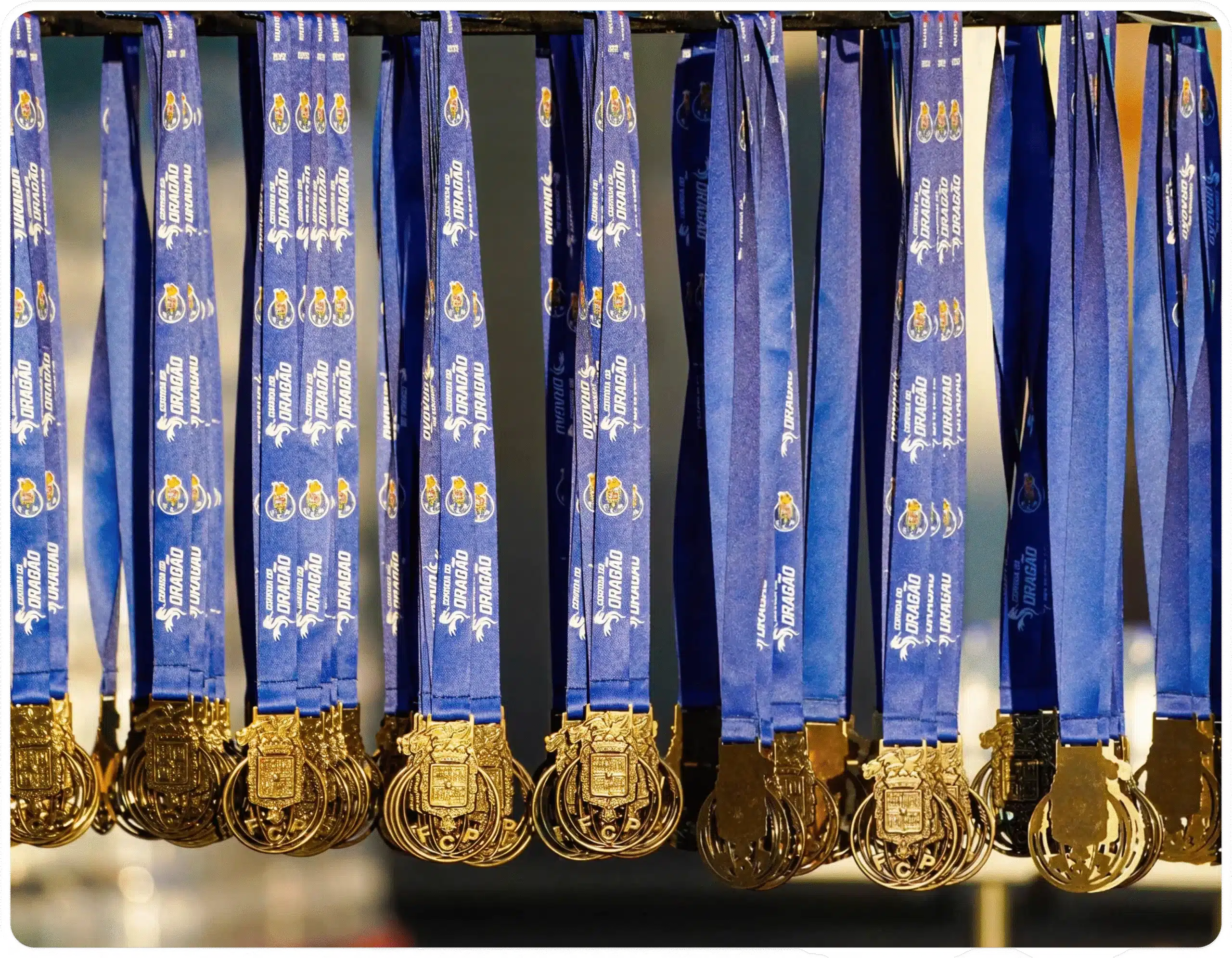 Várias medalhas da Corrida do Dragão penduradas. Cordão azul e medalha dourada.